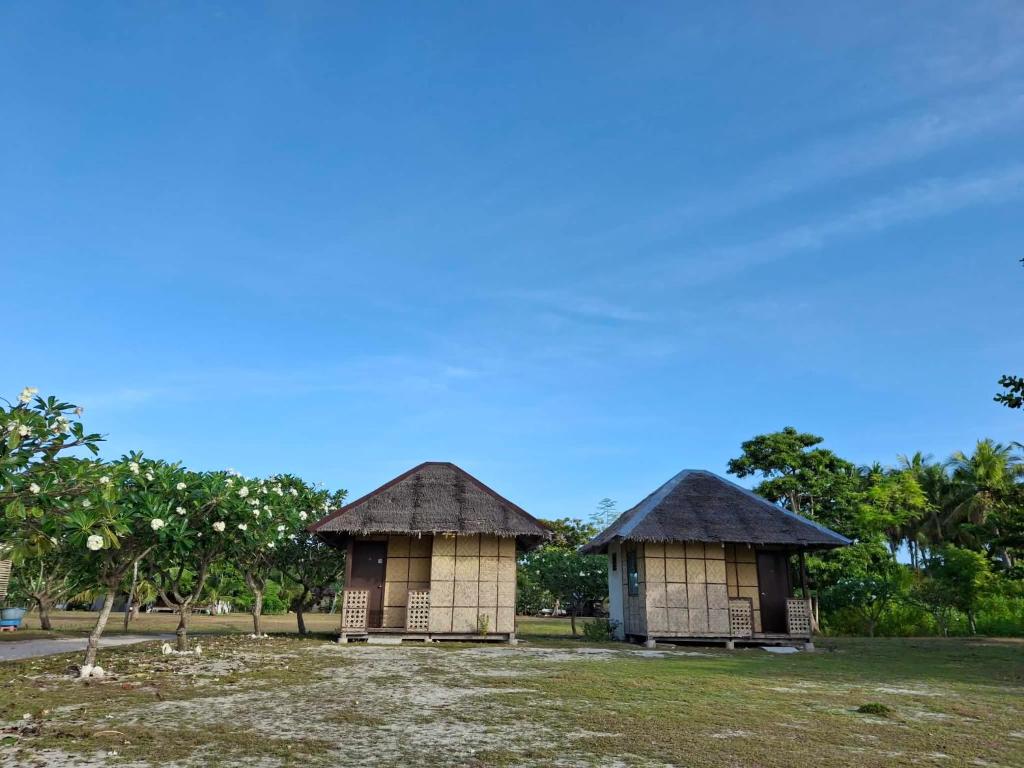 two small huts sitting in a field with trees at Dapearl Cottage in Baclayon