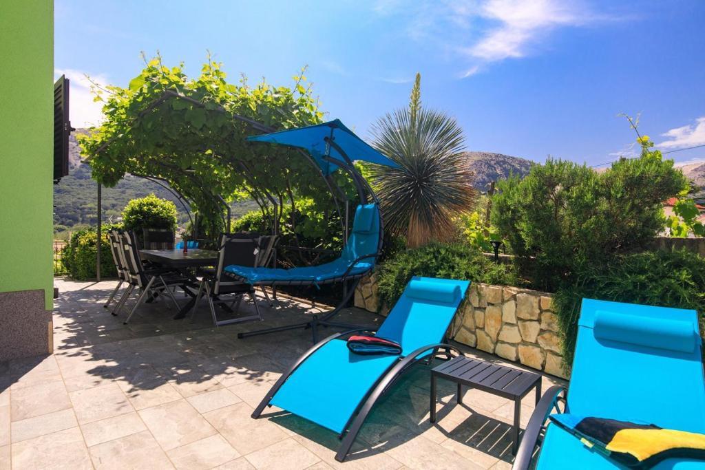 eine Terrasse mit Stühlen, einem Tisch und einem Sonnenschirm in der Unterkunft House Zrile with garden and jacuzzi in Baška