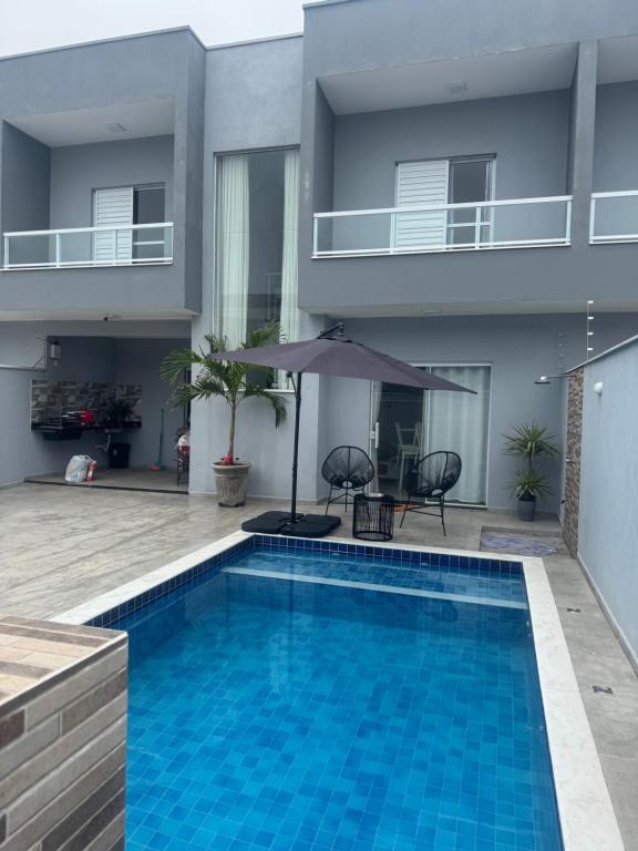 a swimming pool in front of a house with an umbrella at Casa beira Mar in Itanhaém