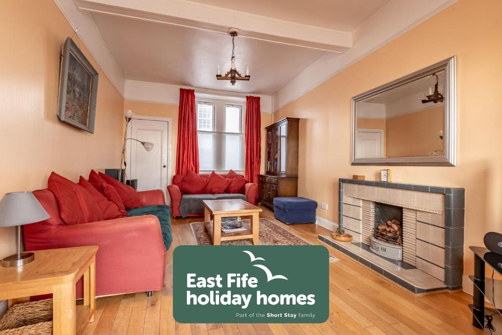 a living room with a red couch and a fireplace at Appleton House - Lower Largo in Lower Largo
