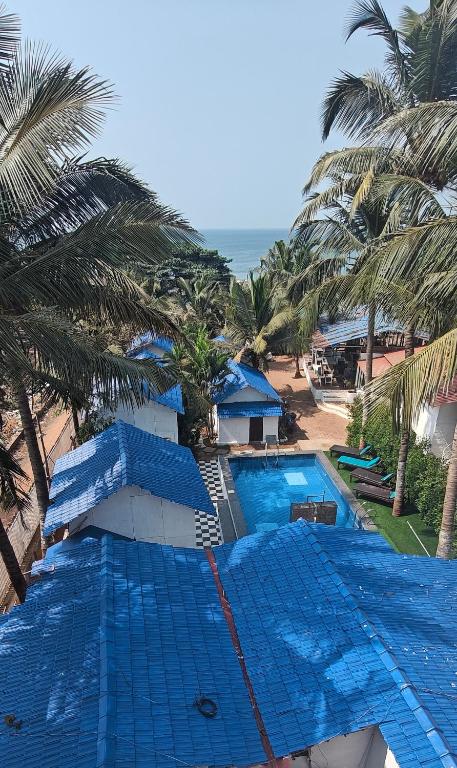 a resort swimming pool with palm trees and the ocean at Beachouse Beachfront Cottages And Suites in Calangute