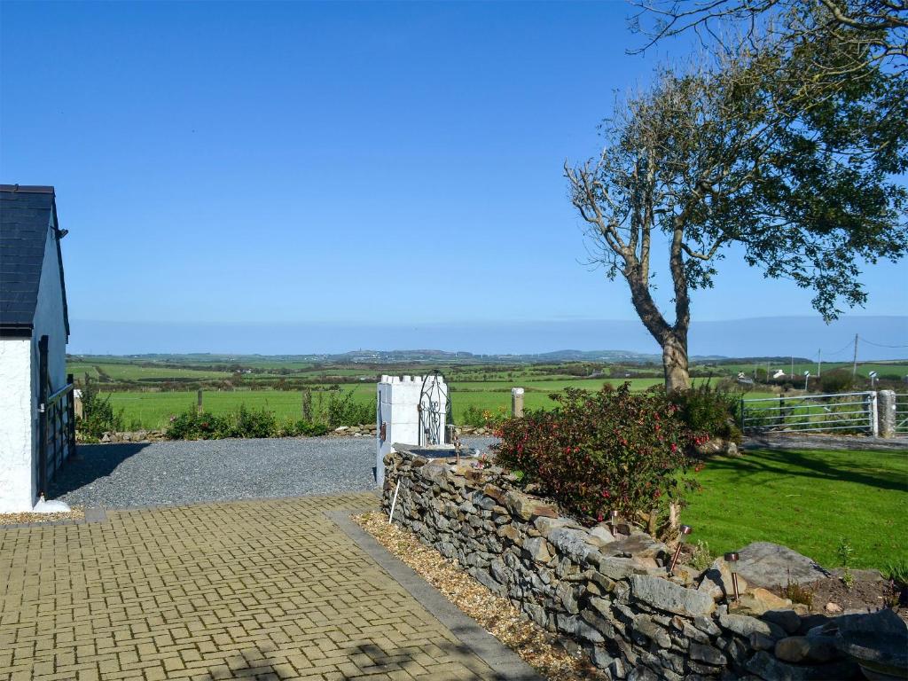 a stone wall next to a house and a tree at Penrhos Bach in Llanerchymedd