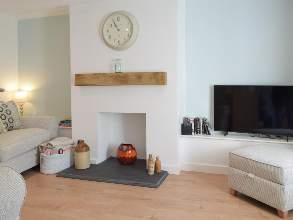 a living room with a fireplace with a clock on the wall at Snowdrop Cottage in Fishguard
