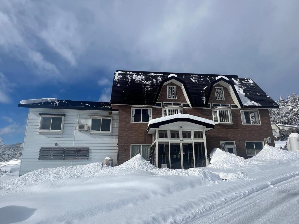 a house with snow on the ground in front of it at Togari Sunshine Lodge in Iiyama