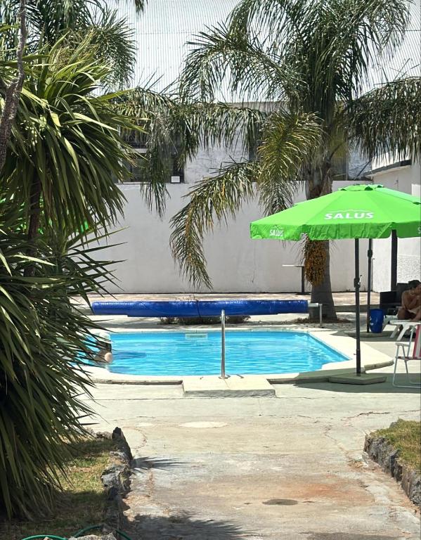 a swimming pool with a green umbrella and a table and a chair at Piriápolis Hostel & suites in Piriápolis