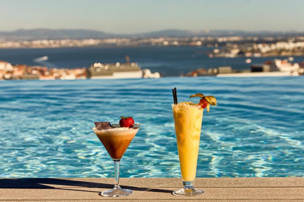 Two cocktails rest beside an infinity pool overlooking Lisbon’s waterfront.