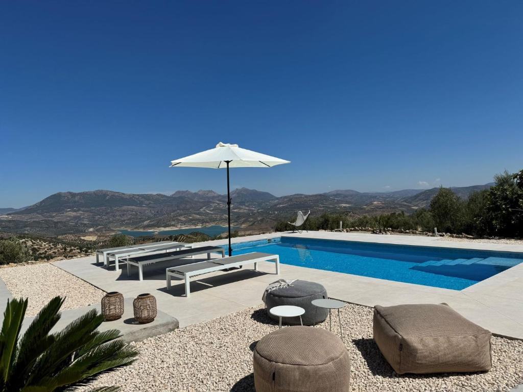 a pool with an umbrella and some chairs and a table at Casa Horizonte in Iznájar