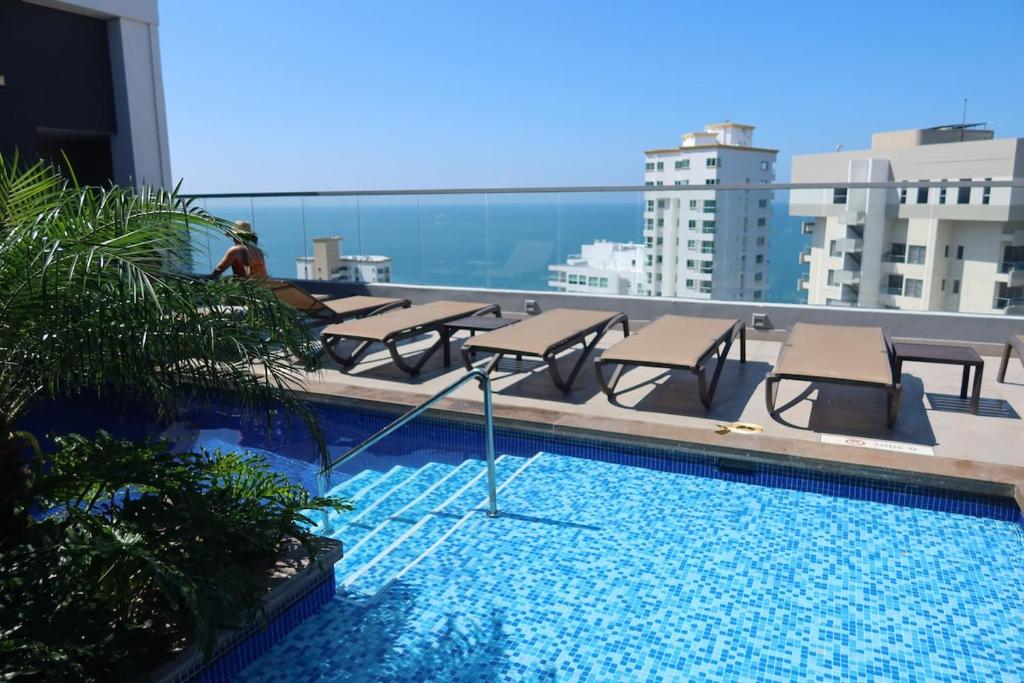 a pool with chairs and tables on top of a building at Rodadero Ocean View Luxury Apt with Rooftop Pool in Taganga