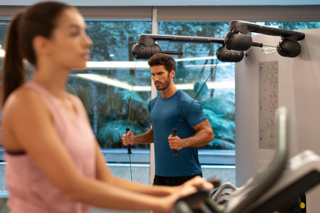 A promotional gym scene showing cardio and cable training beside large windows.