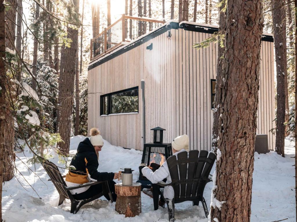 three people sitting in the snow in front of a cabin at Domaine FORESIA in Saint-Alexis-des-Monts
