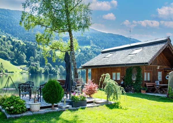 a cabin with a table and chairs in front of a lake at Seehütte Tamberger in Feld am See