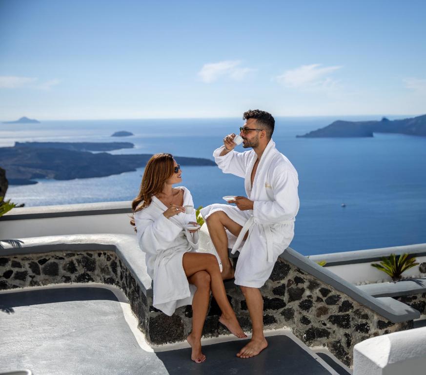 a man and woman in white suits sitting on a ledge at Pegasus Spa Hotel in Imerovigli