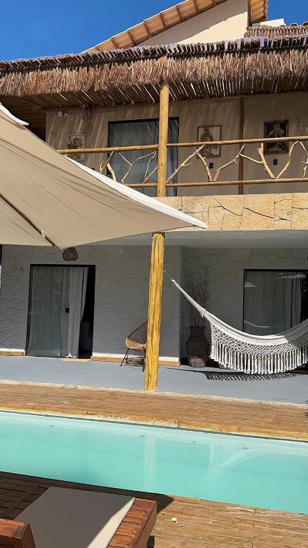 a house with a hammock next to a swimming pool at Suítes House Refúgio Fortim in Fortim