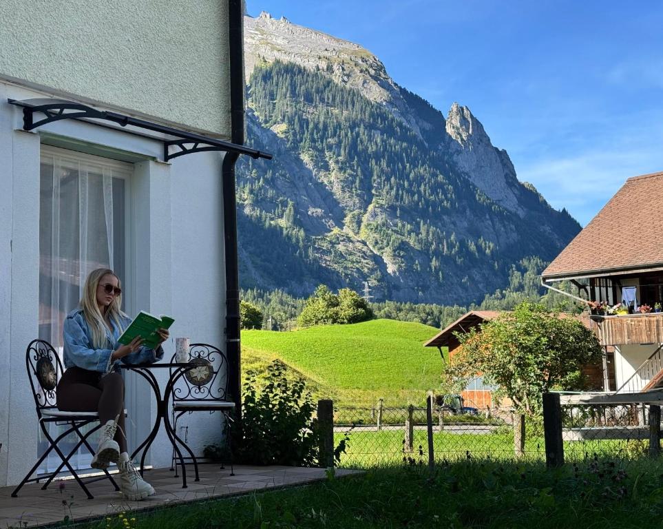 a woman sitting on a bench reading a book with a mountain at Mountain View Apartment in Kandersteg