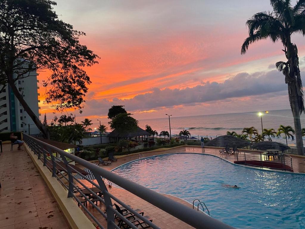 a resort swimming pool with a sunset in the background at Apartamento en Tonsupa - Torresol Tropical in Tonsupa