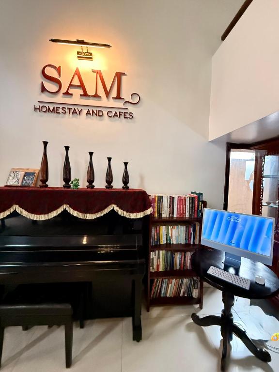 a piano in a living room with a sign on the wall at SAM Homestay and Cafés in Thôn An Hòa
