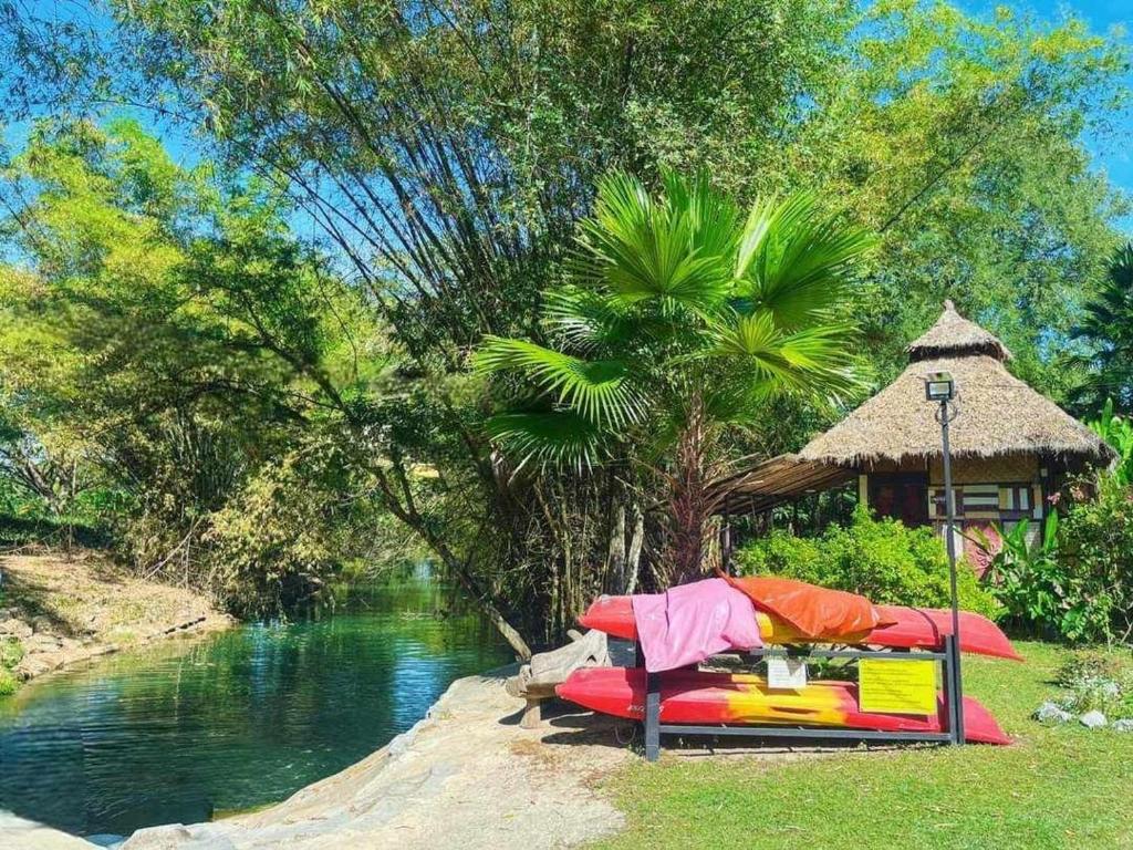 a table and chairs next to a river with a hut at บ้านสุจิปุรี BaanSujipuri in Pak Chong