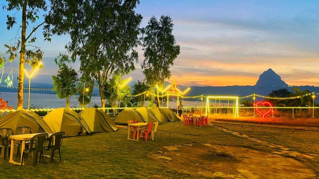 a row of tents with tables and chairs at sunset at Camping At Pawana in Malavli