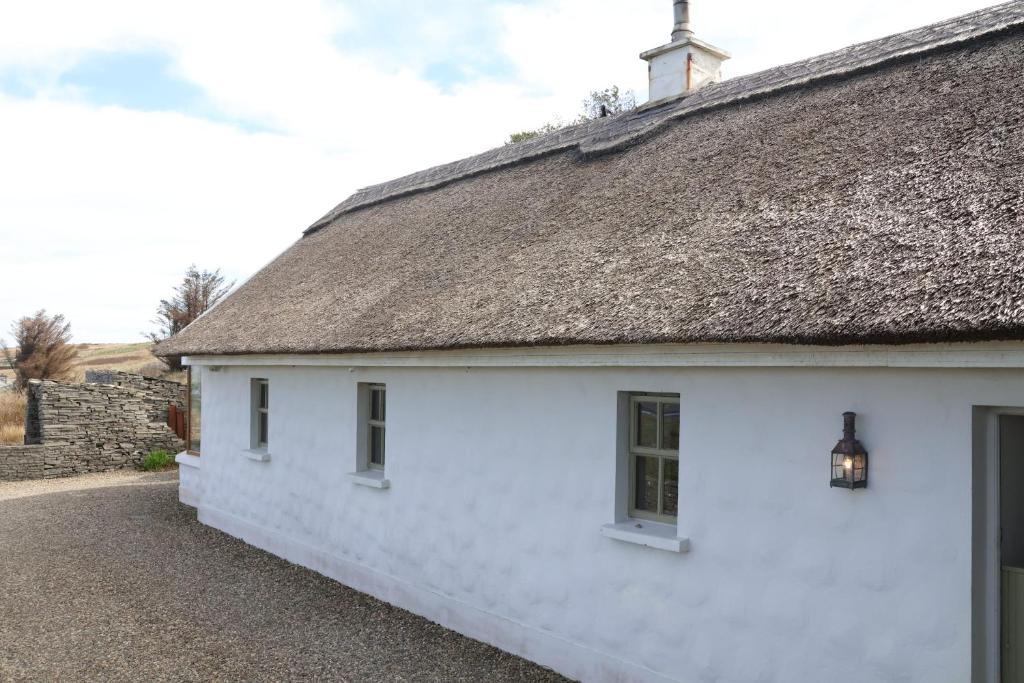 a white cottage with a thatch roof at Storytellers Cottage in Doolin