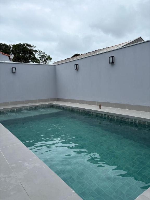 a swimming pool with a white wall and blue water at Casa com piscina praia do ervino in São Francisco do Sul