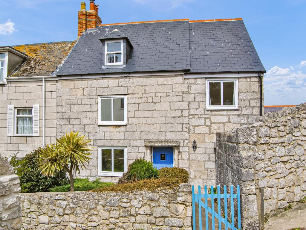 a stone house with a blue door and a stone wall at Pebbles in Castletown