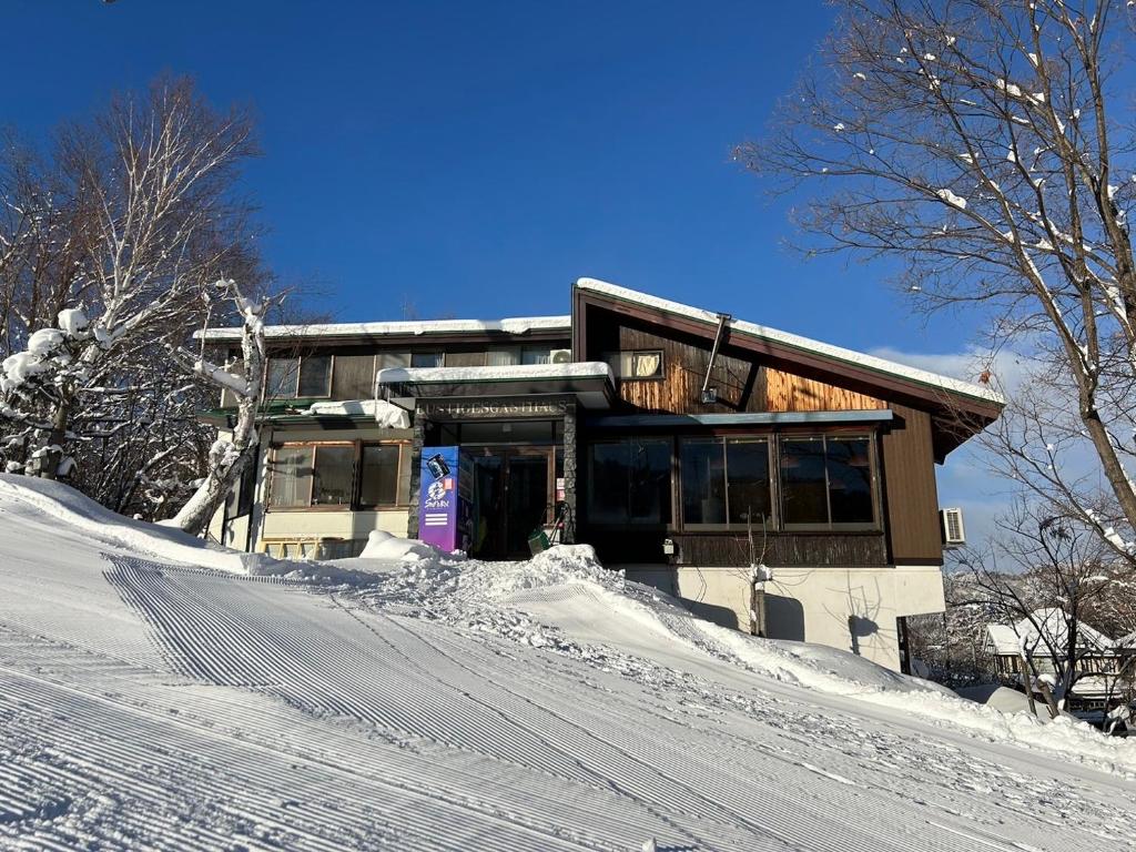 a house on a snow covered hill with a building at ゲストハウスルスティゲス in Kijimadaira