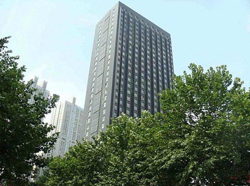 un edificio alto con árboles delante de él en Homy Inns Mu Ma, en Nanjing