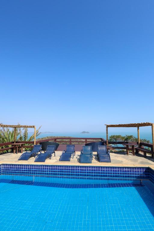 a swimming pool with chairs and the ocean in the background at Pousada Mirante dos Papagaios in Búzios