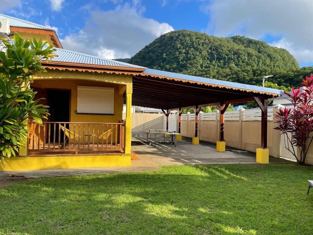 a yellow building with a porch with a mountain in the background at Villa Soleil des Caraïbes in Gourbeyre