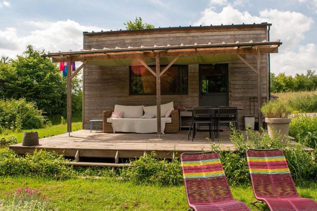 a wooden deck with a couch and chairs on it at Tiny house gite bucolique Brocéliande Hébergement insolite et centre bien être in Saint-Brieuc-de-Mauron