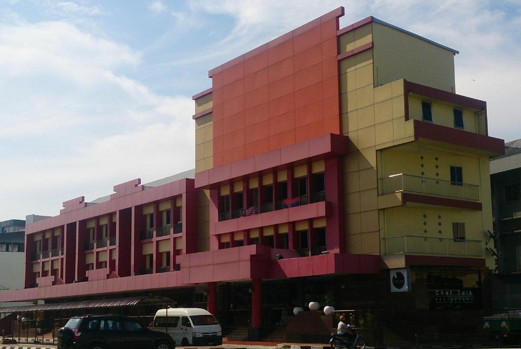 un edificio rosa con coches estacionados frente a él en Hotel & Apartment Ambassador 3 en Labuan