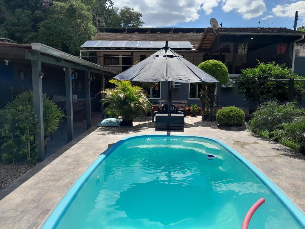 a swimming pool in front of a house with an umbrella at Recanto Romig in Pomerode