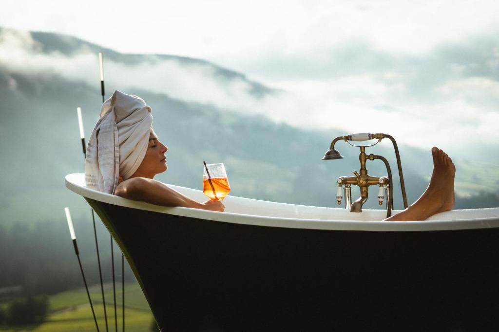 a woman sitting in a bath tub with a glass of wine at Gailerhof Boutique Hotel B&B Dolomites in Monguelfo