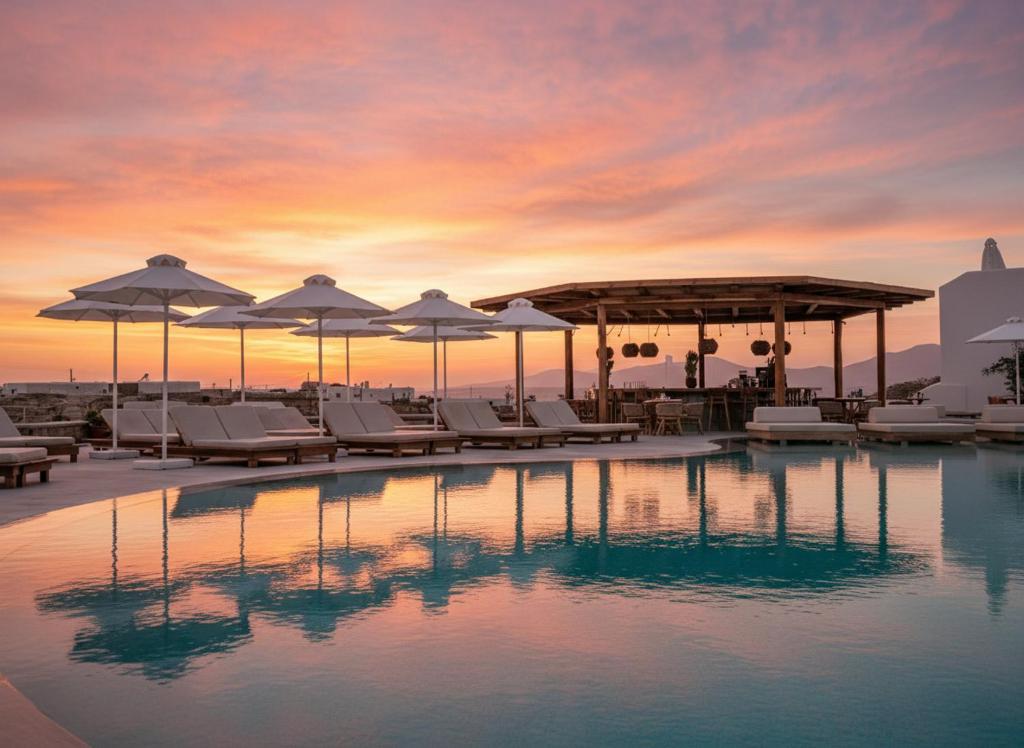 a pool with lounge chairs and umbrellas at sunset at San Antonio Summerland in Mikonos