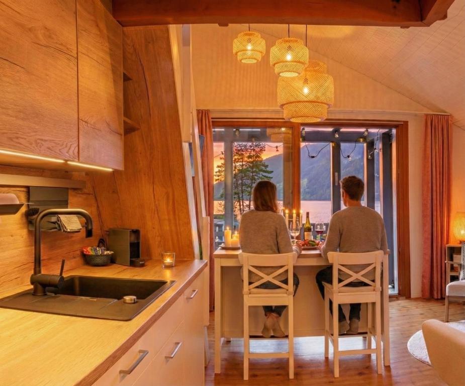 Zwei Personen sitzen an einer Küchentheke und schauen aus dem Fenster. in der Unterkunft Sunsethüsli in Därligen