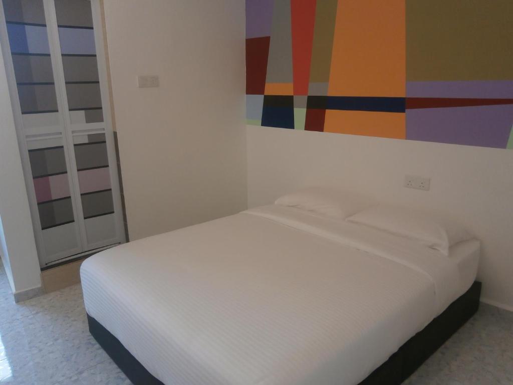 een wit bed in een kamer met een schilderij aan de muur bij F.M GUESTHOUSE in Kampong Darat Tanah Puteh