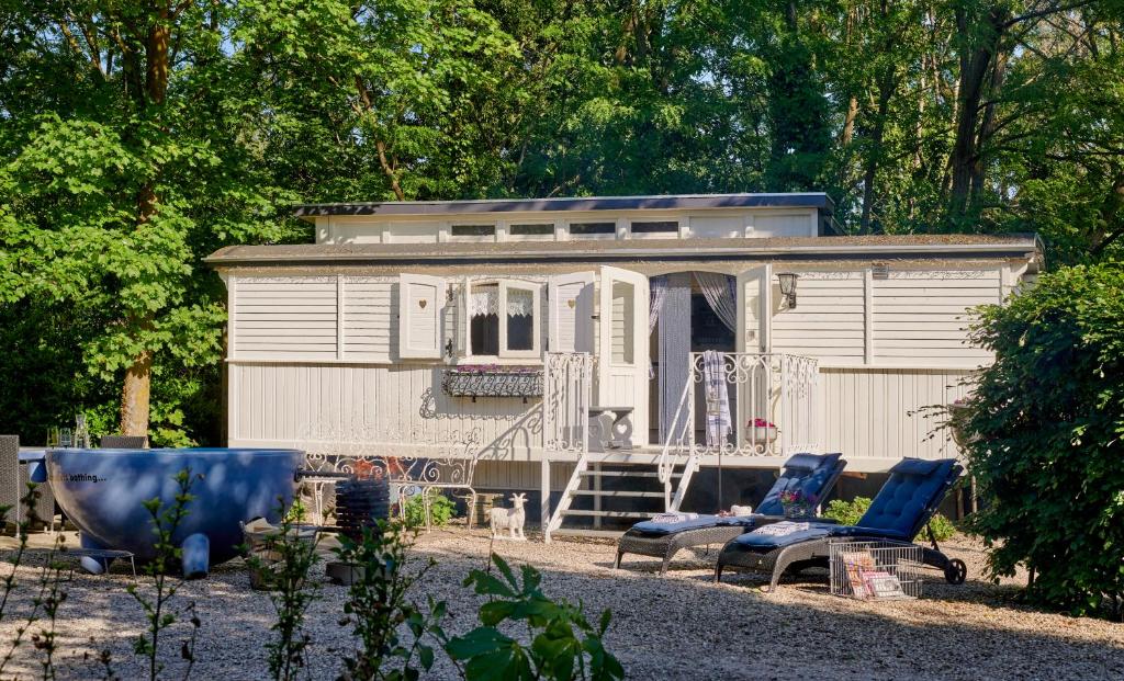 a tiny house with chairs and a porch in front of it at Pipowagen de Luxe, prive hottub en zwembad in Heythuysen