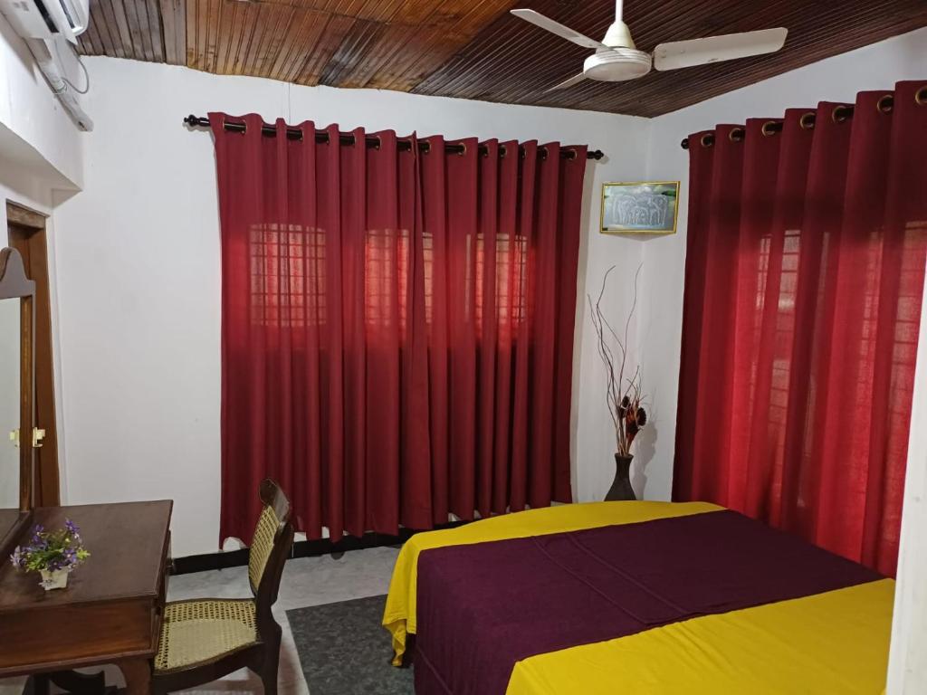 a bedroom with red curtains and a yellow bed at Solar House Hotel in Dickwella