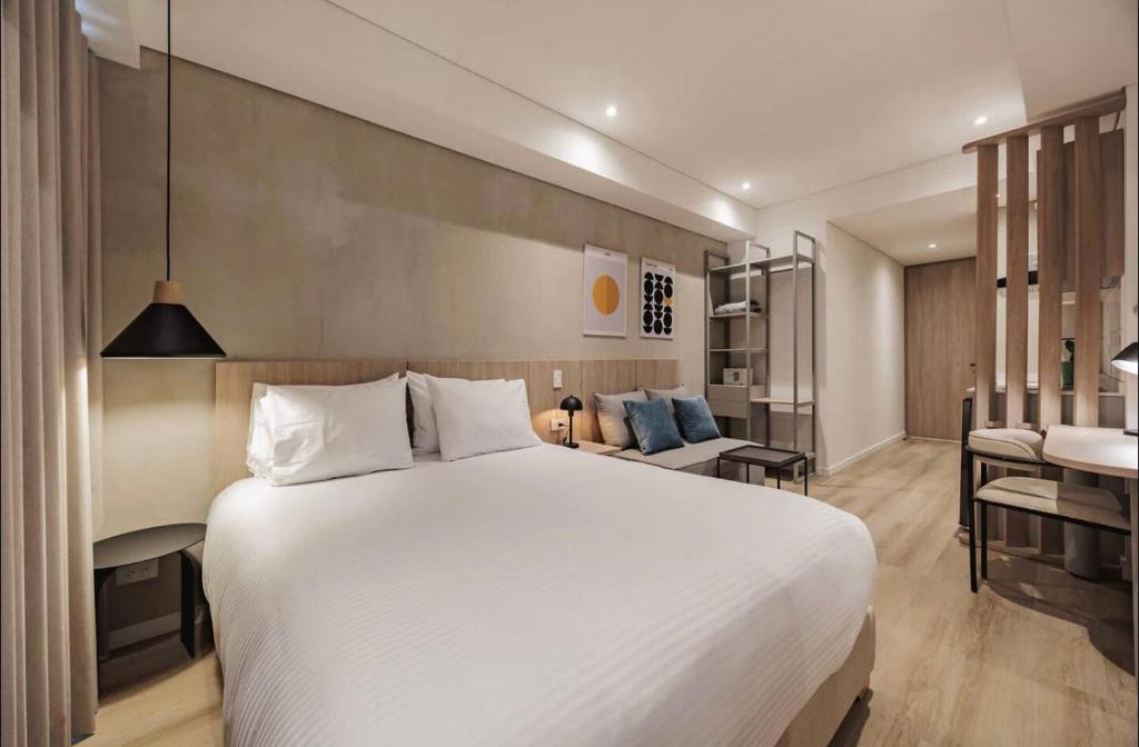a bedroom with a large white bed and a living room at Laureles Studios - Tomas in Medellín