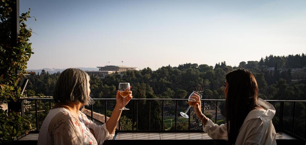 two women holding up glasses of wine on a balcony at Biazi Hotel in Jerusalem