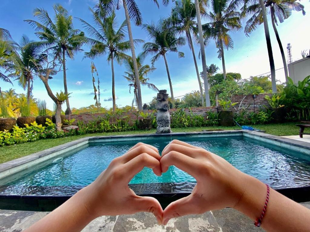 a person making a heart shape with their hands in front of a pool at Shima House in Sukawati