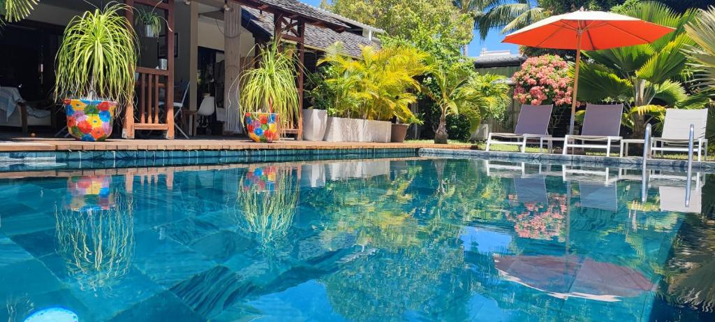 a swimming pool with an umbrella and a house at SWEET ISLAND logement petit déjeuner inclus in Rivière Noire