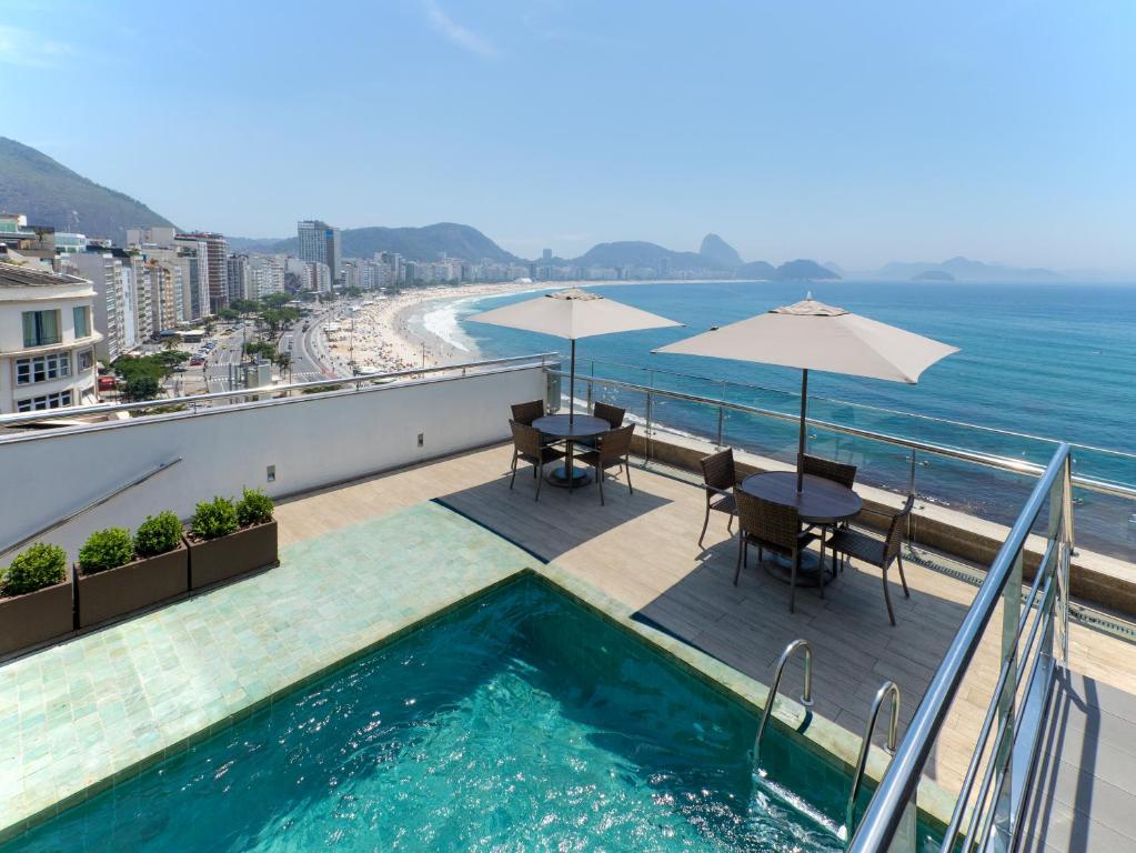 un balcón con piscina, mesas y sombrillas en Orla Copacabana Hotel en Río de Janeiro