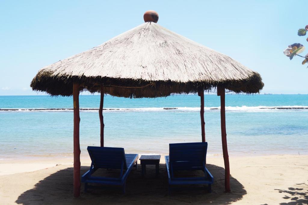 duas cadeiras e uma mesa debaixo de um guarda-sol de palha na praia em Hotel Robinson Plage em Lomé