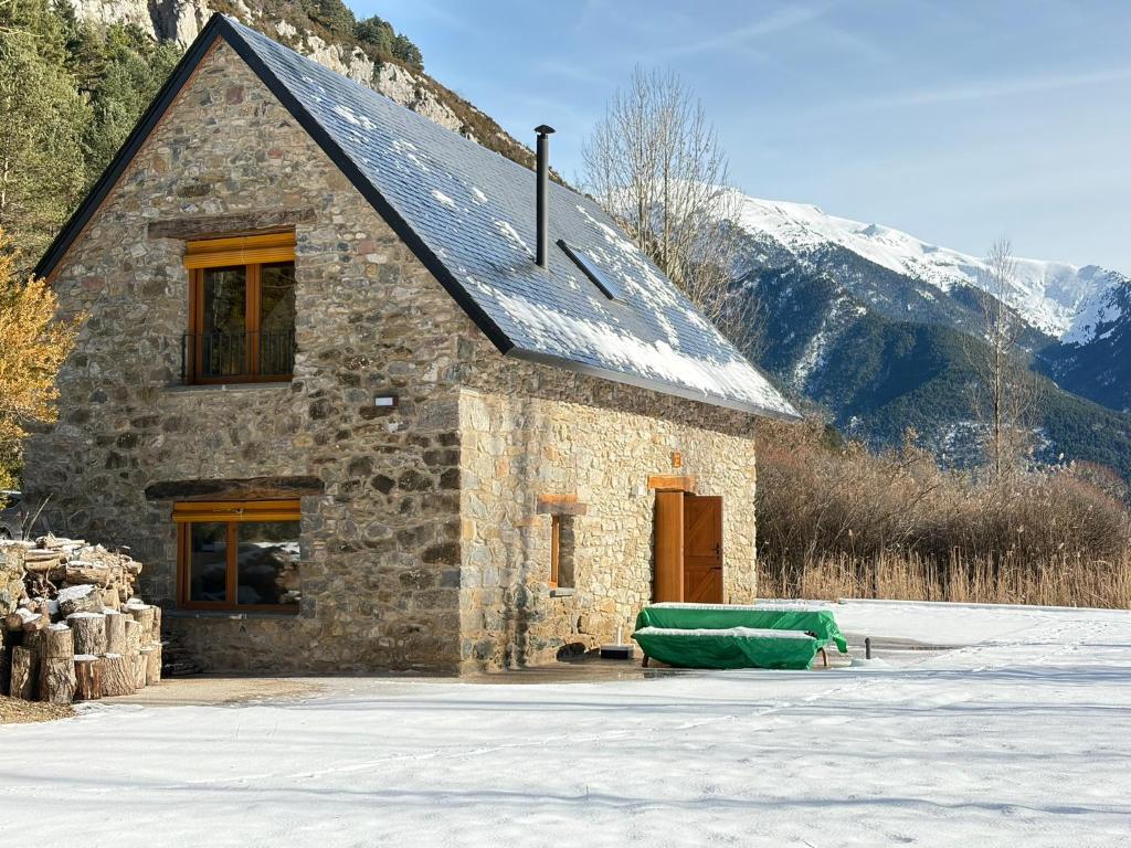 a small stone building with a green blanket in the snow at Borda del Llano in Bielsa