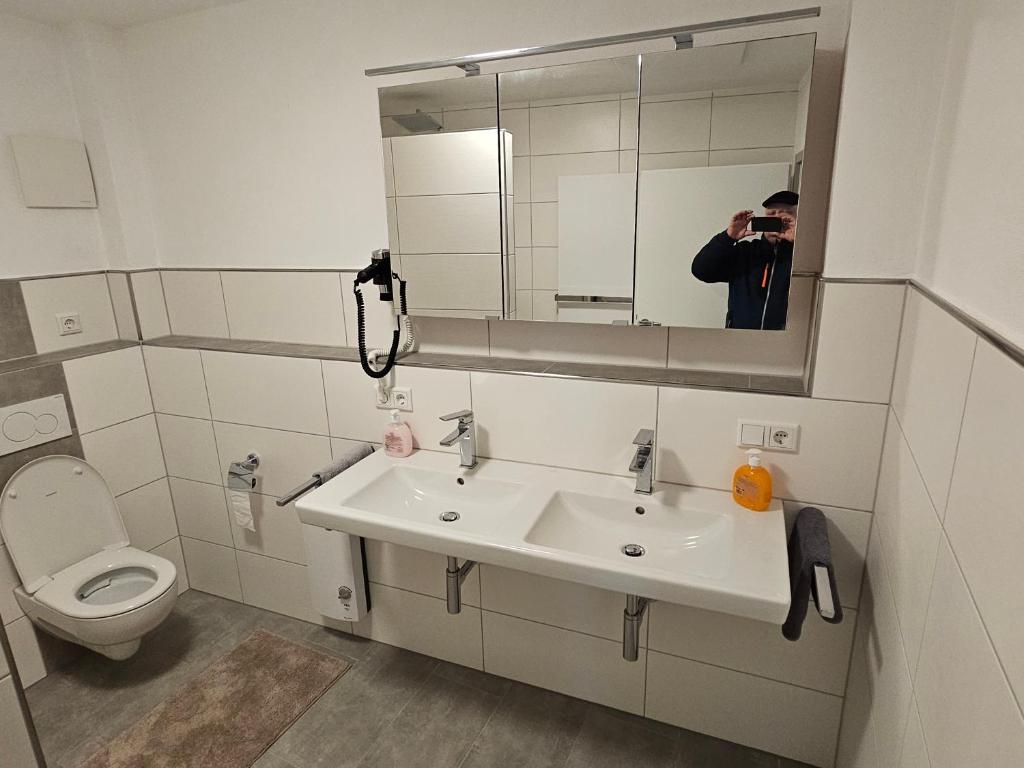 a man taking a picture of a bathroom with a sink at Torwirt Apartments in Herrieden