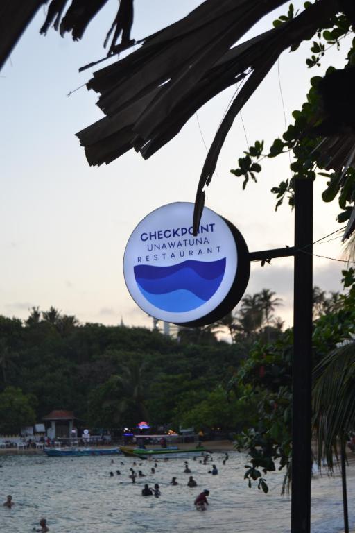 a sign at a beach with people in the water at Check Point in Unawatuna