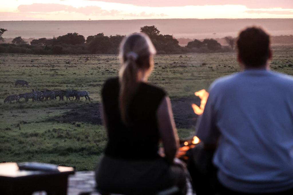 a man and woman looking at a herd of zebras at Entalet Mara Camp in Talek