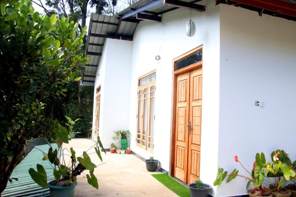 a white house with a wooden door and some plants at Riverside Bliss Cottage in Demodera