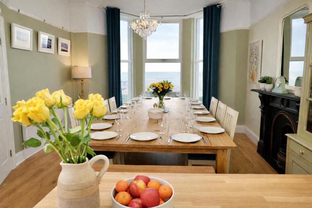 a long dining room table with yellow flowers in a vase at Bay View, Sleeps 18, 7 Bedrooms, 7 Bathrooms, Seafront, Criccieth in Criccieth